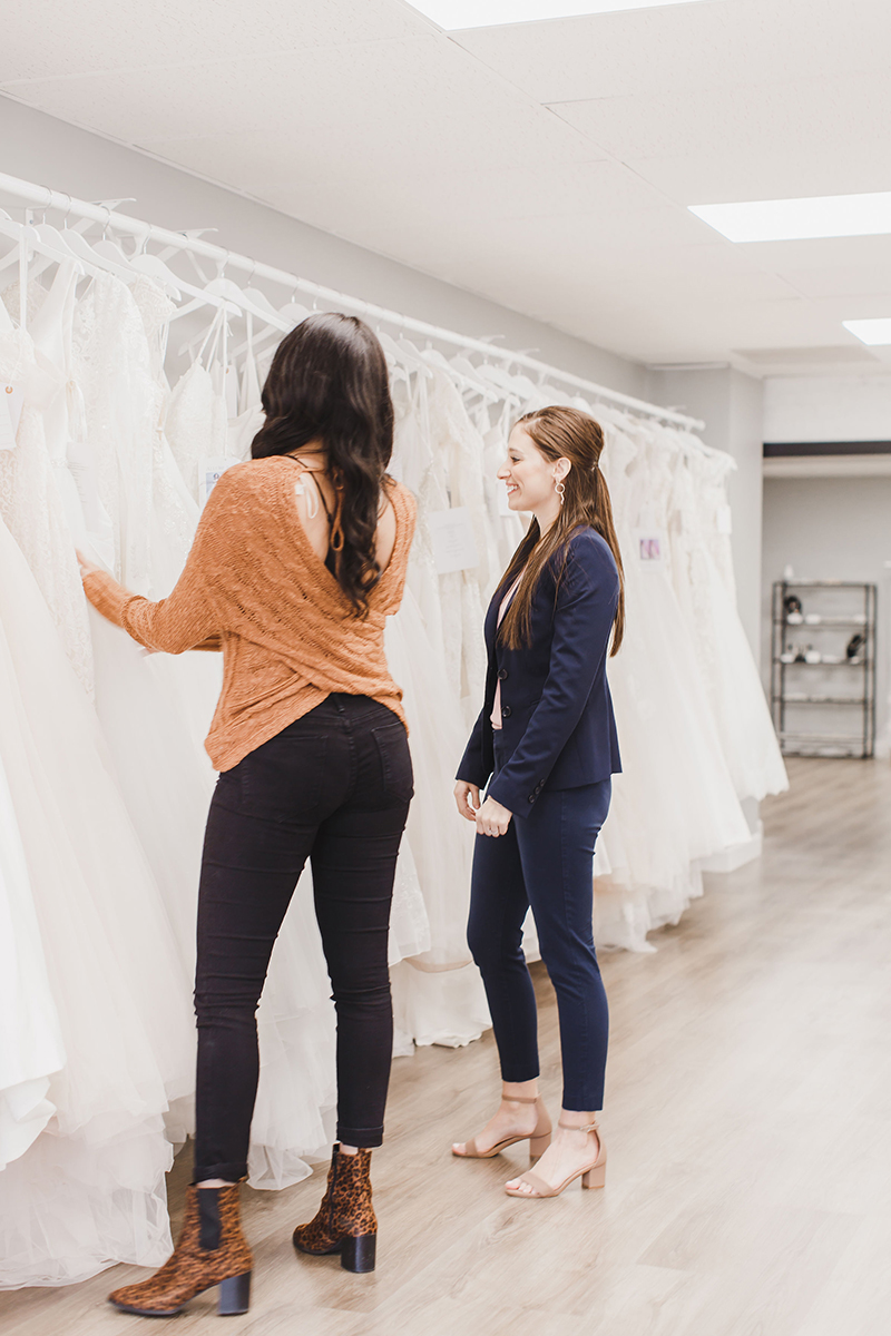 a sales associate and a customer looking at wedding dresses