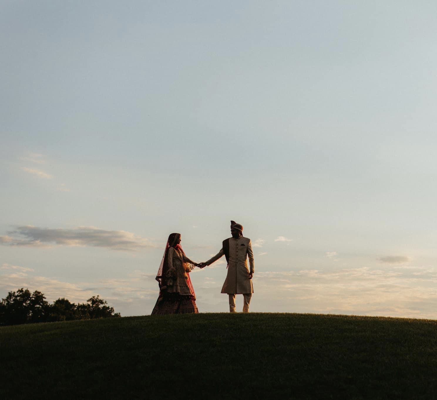 a groom holding his bride's hand standing on top of a hill